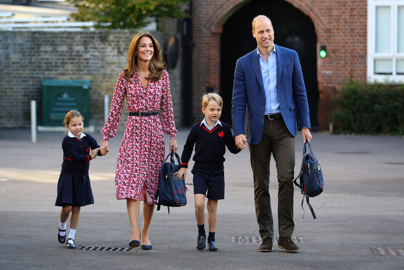 Kate Middleton and Prince William holding hands with their kids and holding backpacks