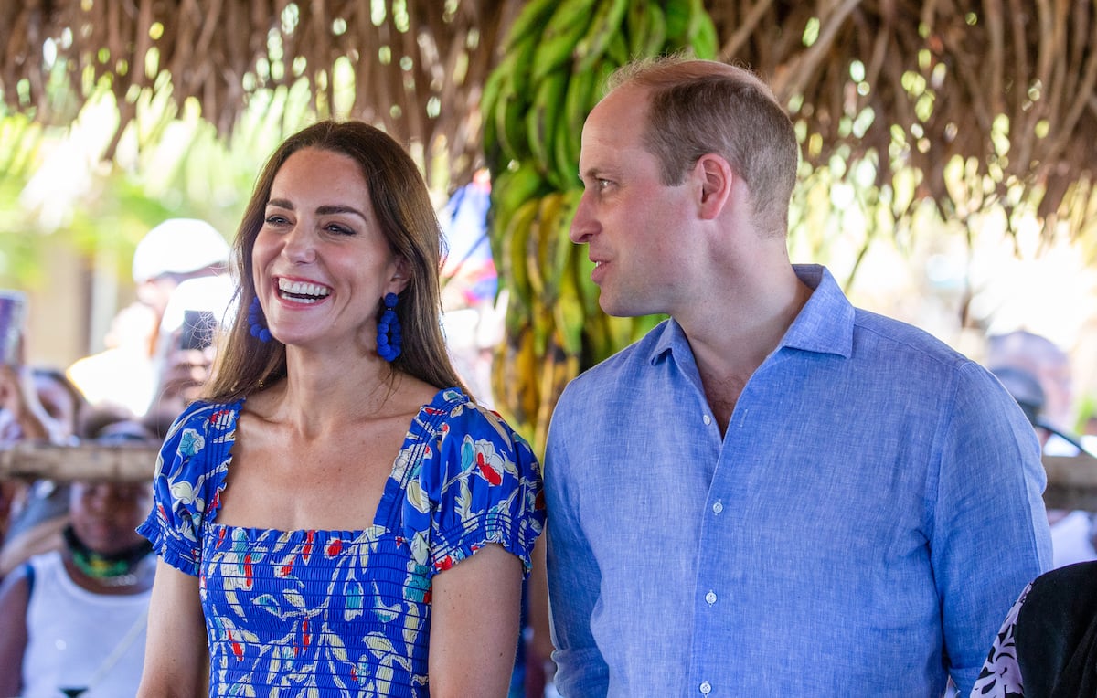 Kate Middleton smiles wearing a blue dress while Prince William looks at her wearing a blue shirt