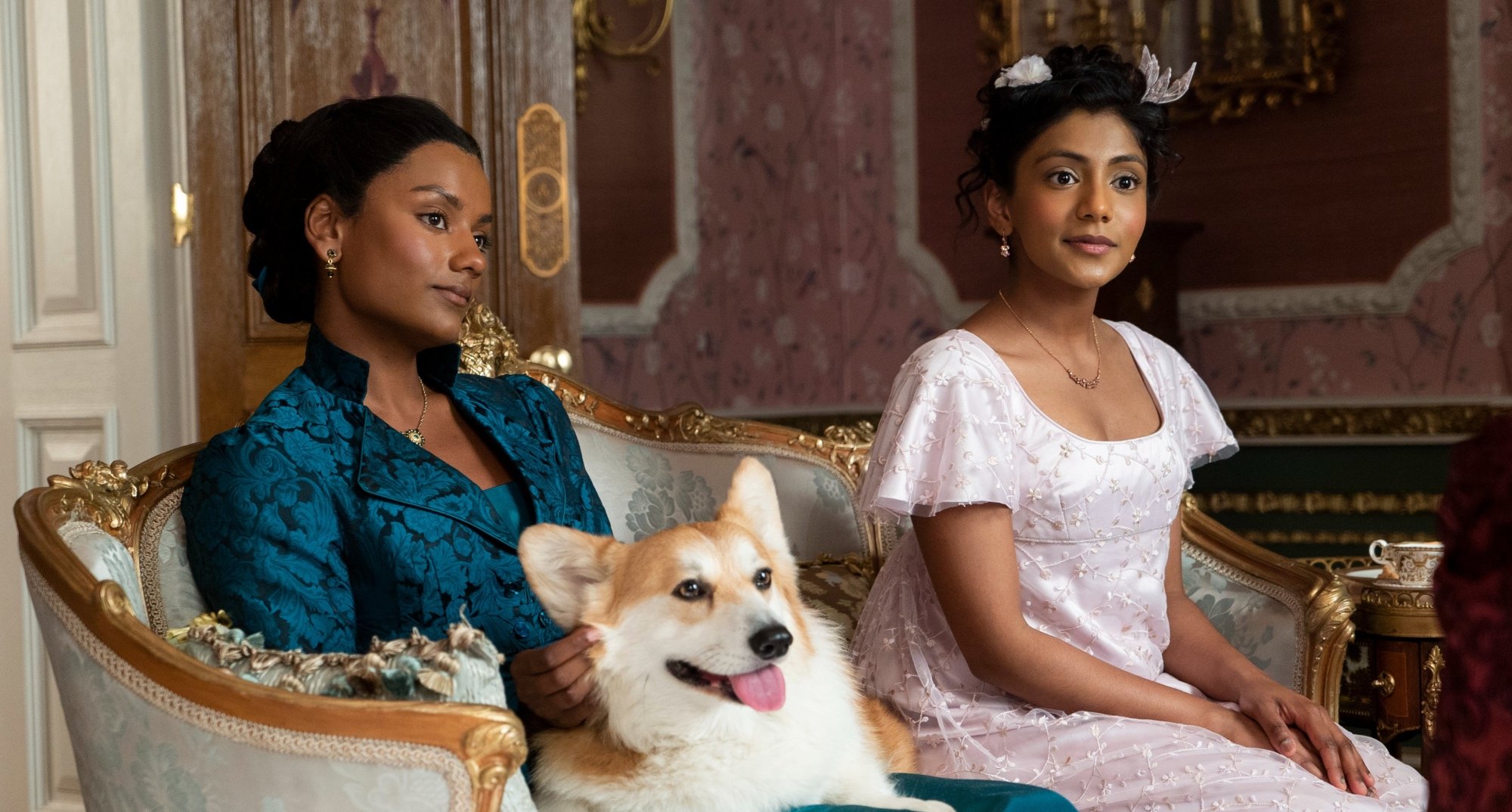 Kate and Edwina Sharma in 'Bridgerton' Season 2 sitting in loveseat with dog.