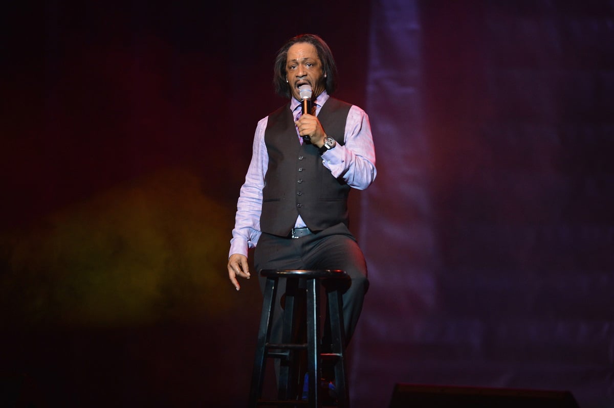 Katt Williams holding a microphone while wearing a purple suit.
