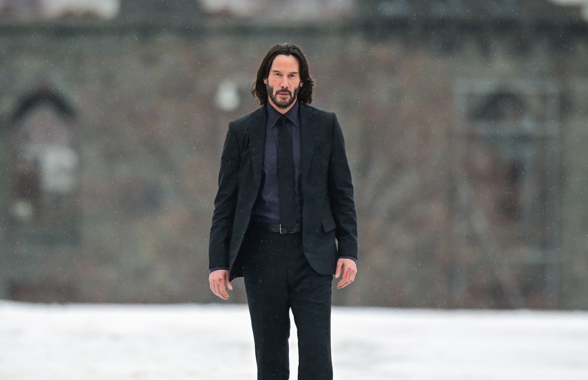 Keanu Reeves posing while wearing an all black suit.
