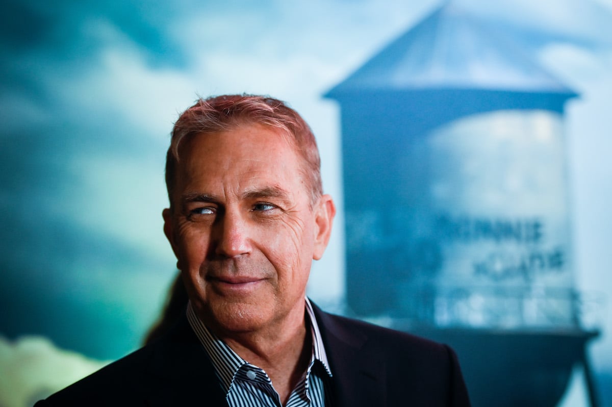 Kevin Costner smiles on the red carpet with a water tower in the background