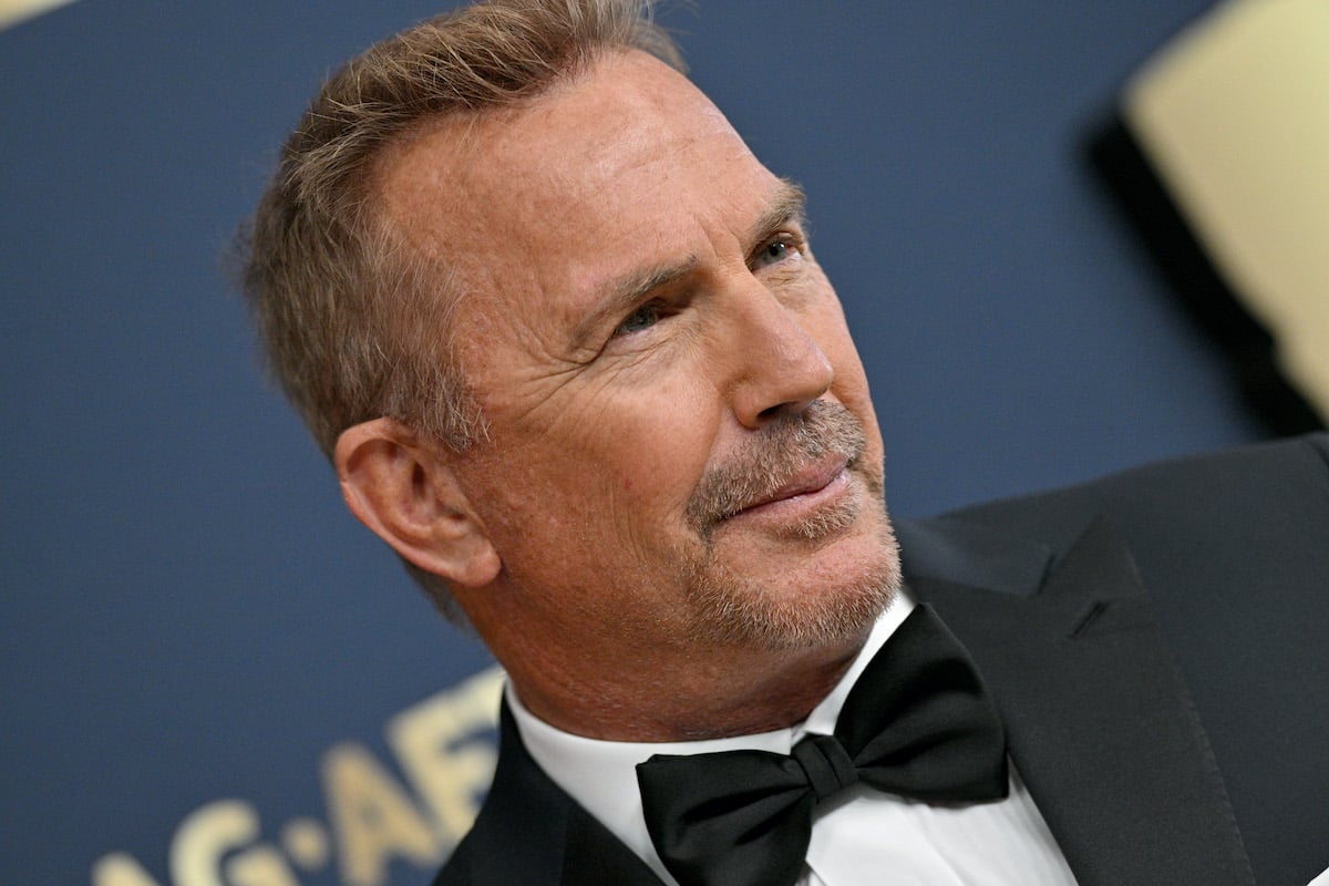 Kevin Costner wears a black suit and smiles