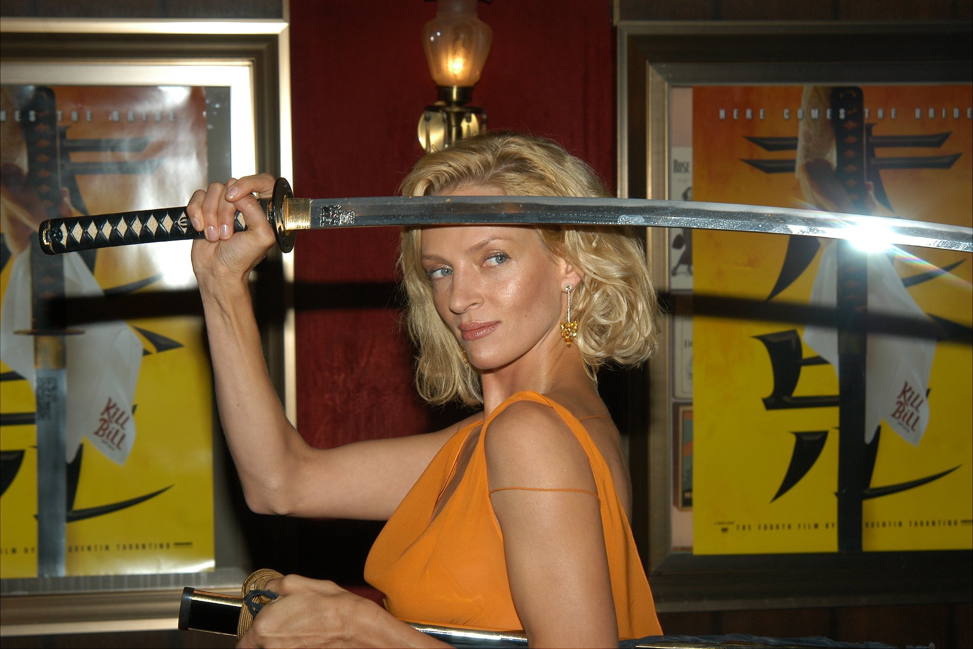 'Kill Bill' star Uma Thurman holding a samurai sword in front of the movie posters