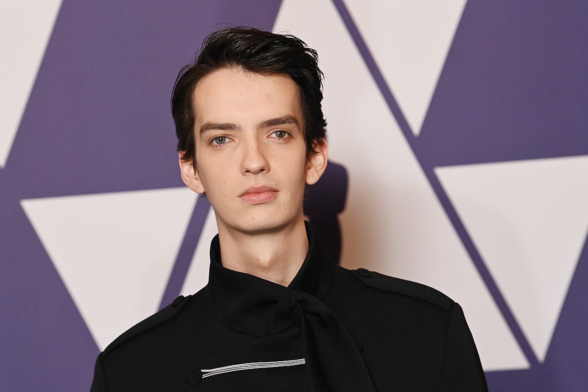 Kodi Smit-McPhee poses in black in front of a purple Academy Awards logo