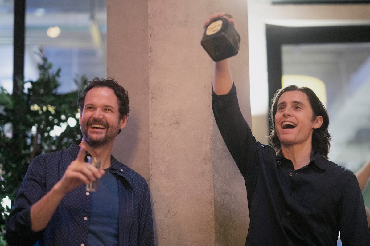 Kyle Marvin smiles while Jared Leto raises his arm in a scene from 'WeCrashed' Season 1 Episode 4: '4.4'