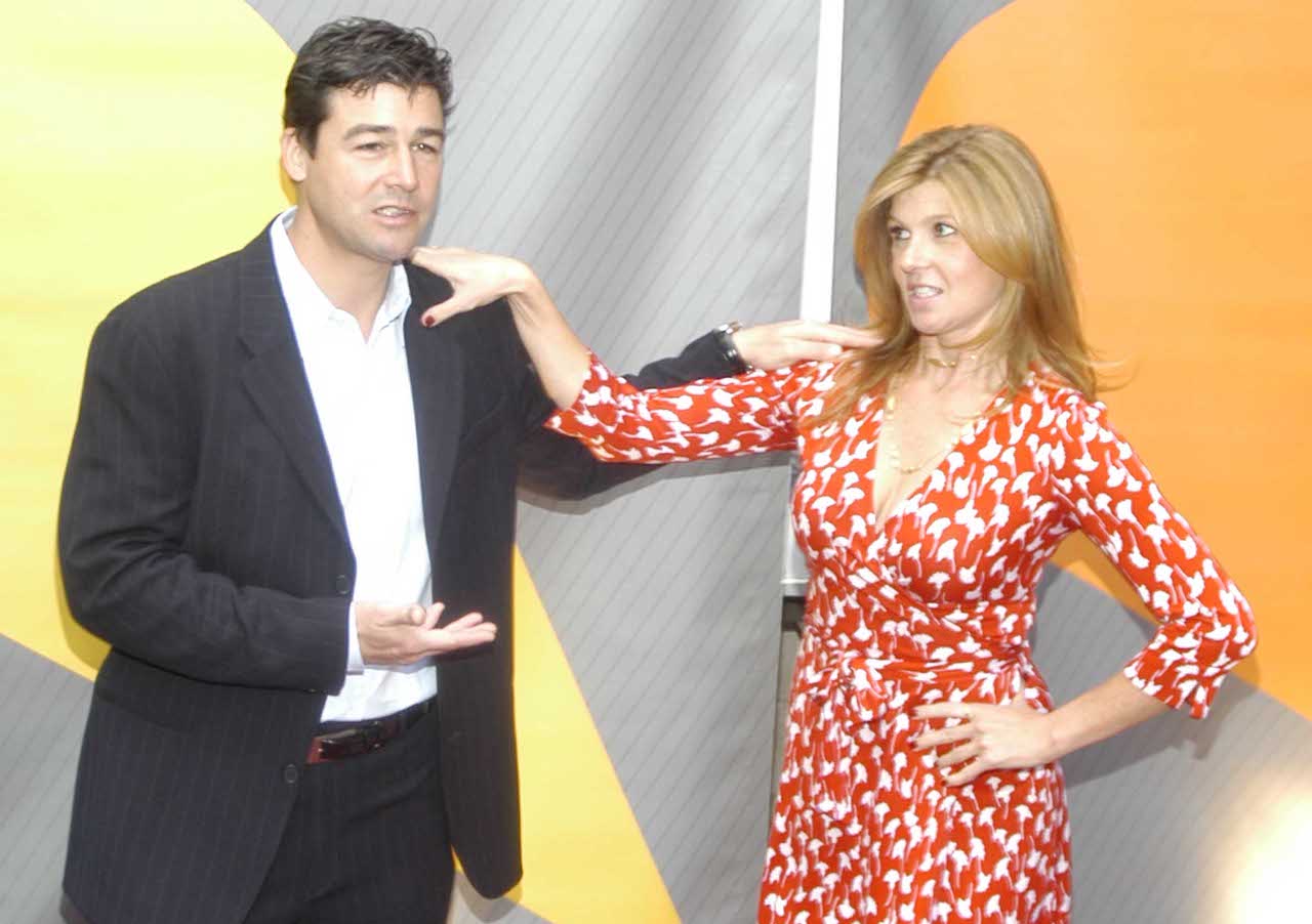 Kyle Chandler in a black suit, standing next to Connie Britton in a red and white dress, each putting a hand on the other's shoulder