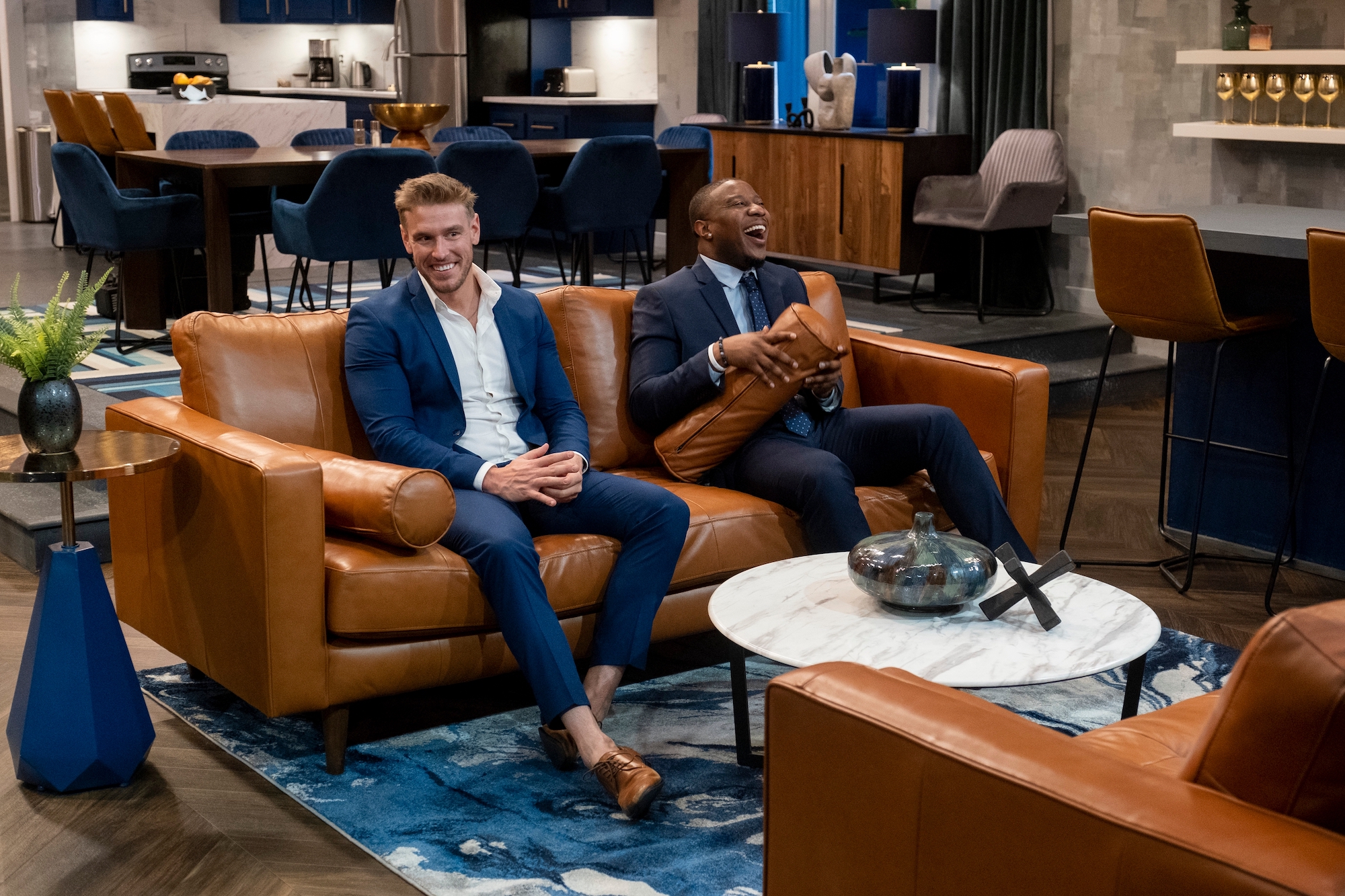 'Love is Blind' Season 2 star Shayne Jansen wearing a blue suit and sitting on a tan couch.