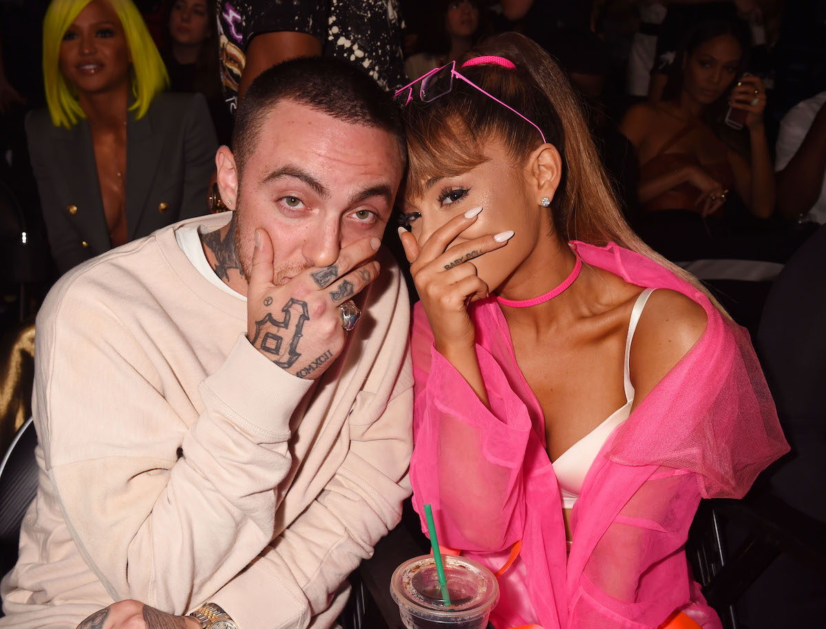 Mac Miller and Ariana Grande pose with their hands over their mouths at an event.