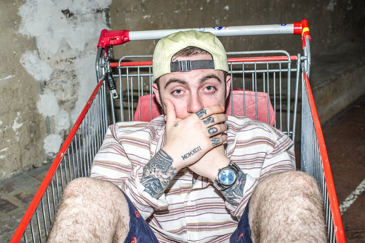 Mac Miller poses in a shopping cart with his hands covering his mouth.