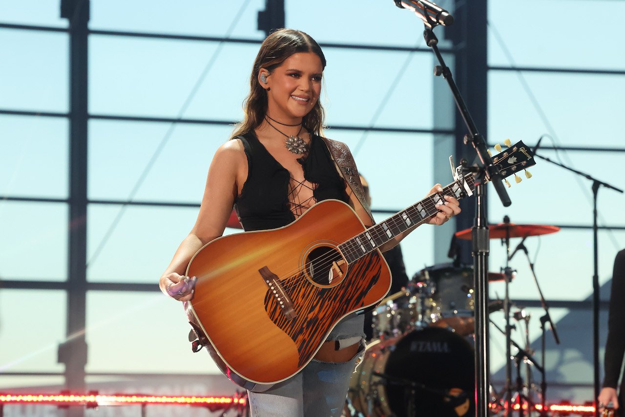 Maren Morris performs onstage in a black tank top and jeans, holding a guitar