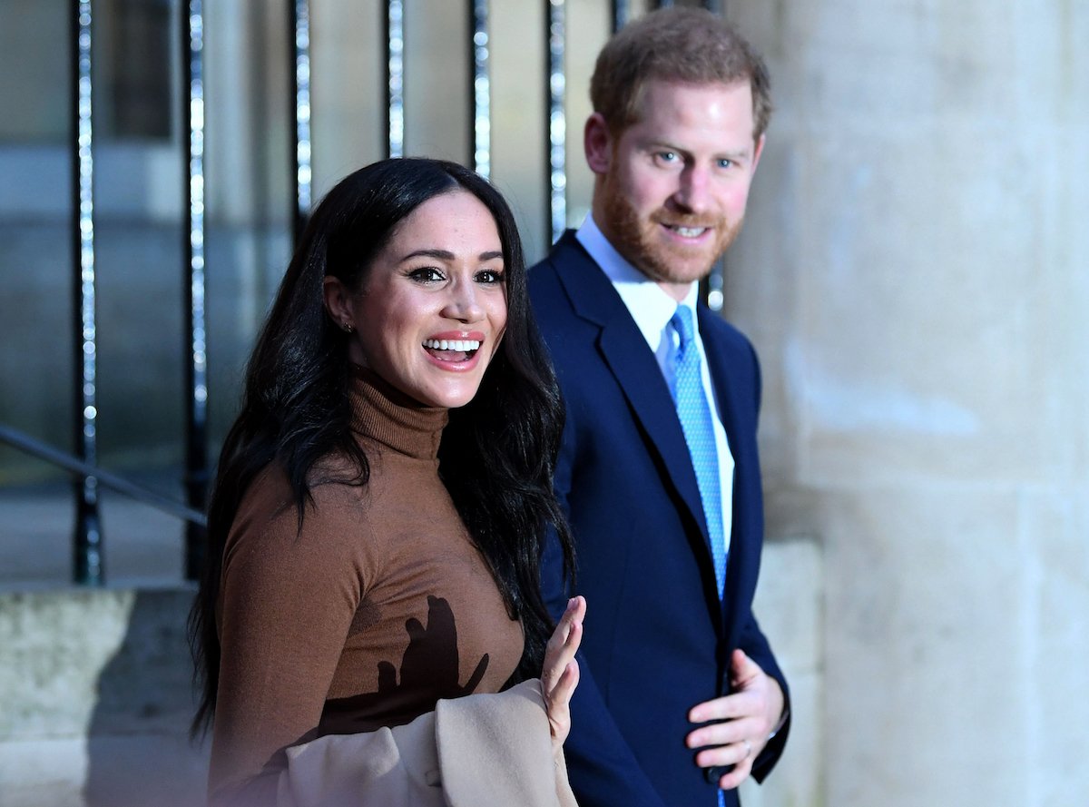 Meghan Markle waves as she exits a building with Prince Harry