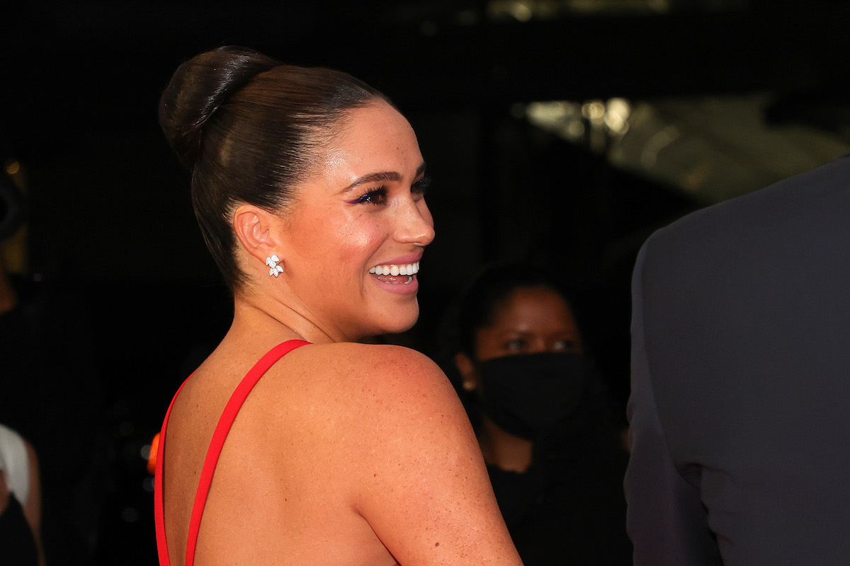 Meghan Markle smiles looking over her shoulder wearing a red dress