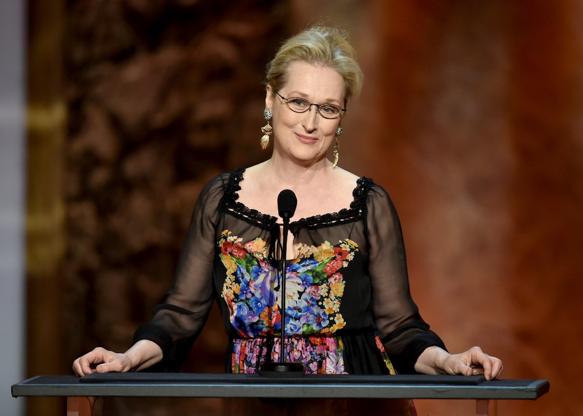 Meryl Streep honoring Jane Fonda for movie career in front of a microphone with her hands on the podium