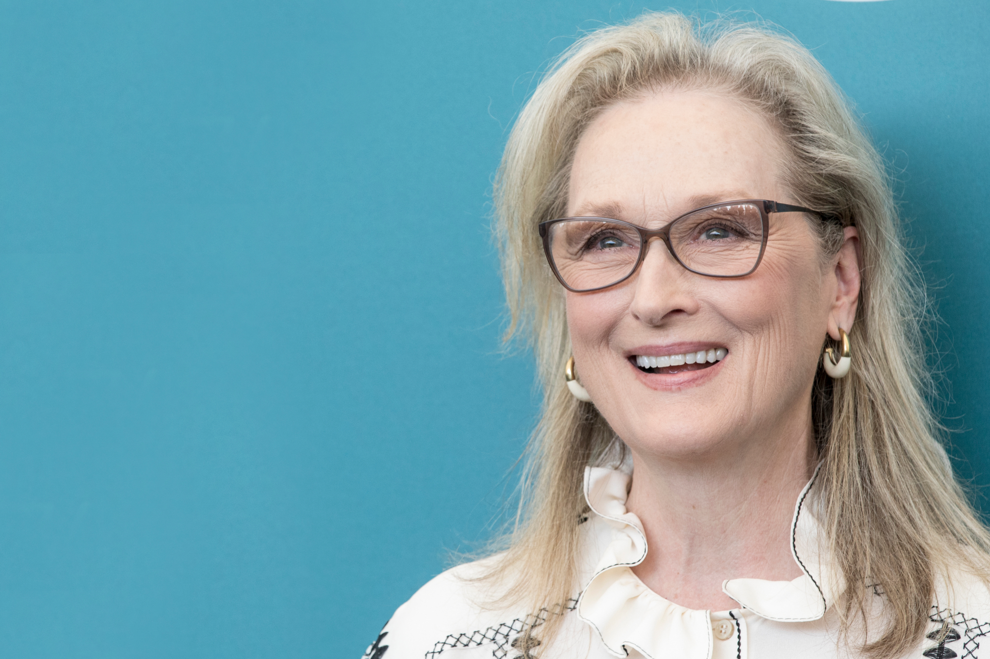 Meryl Streep, star of Woody Allen's 'Manhattan' smiling with glasses in front of blue step and repeat
