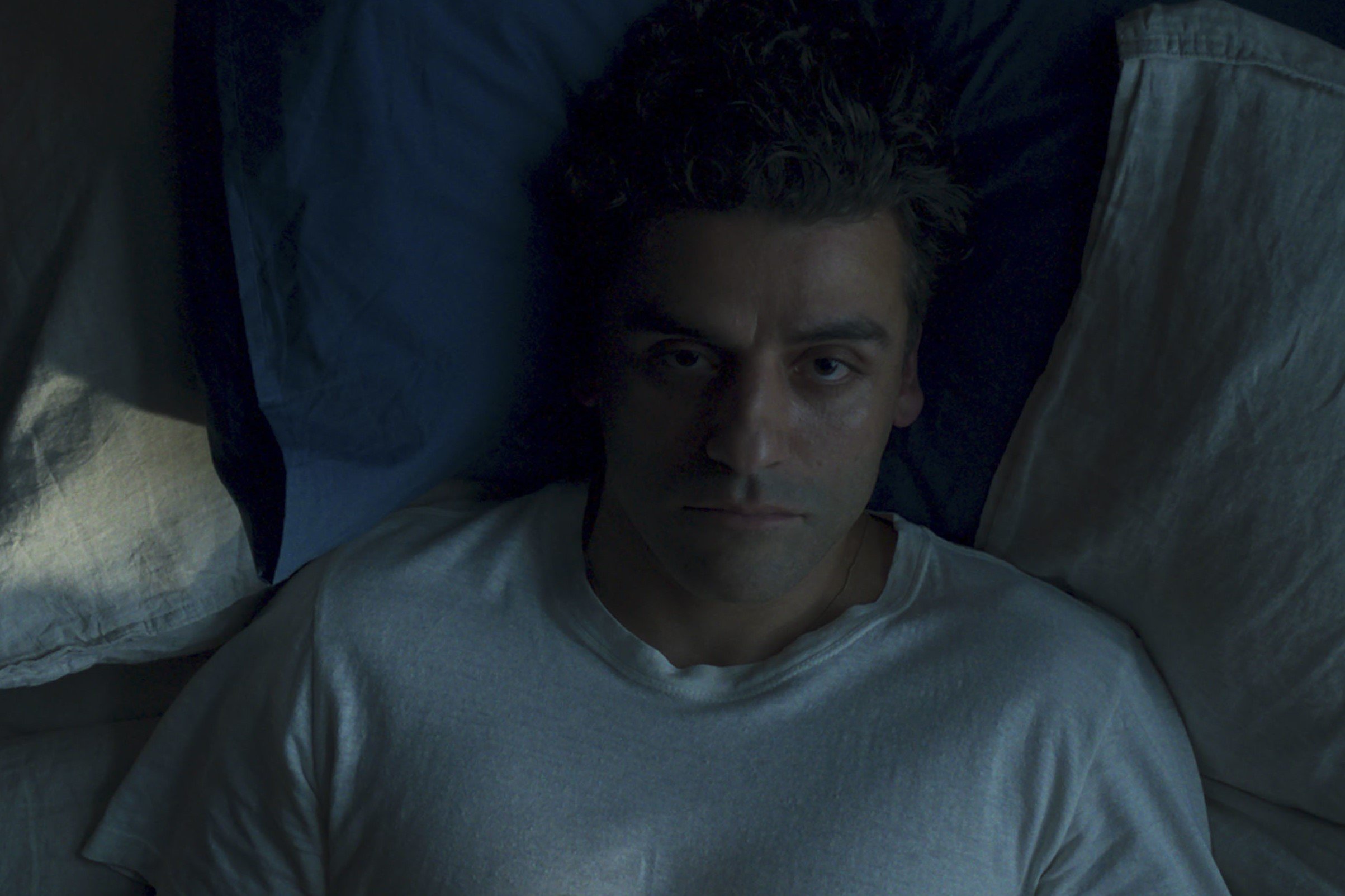 Oscar Isaac, whose brother helped him play multiple characters in 'Moon Knight,' appears in a scene as Steven Grant. Steven lays in beds and wears a white shirt.