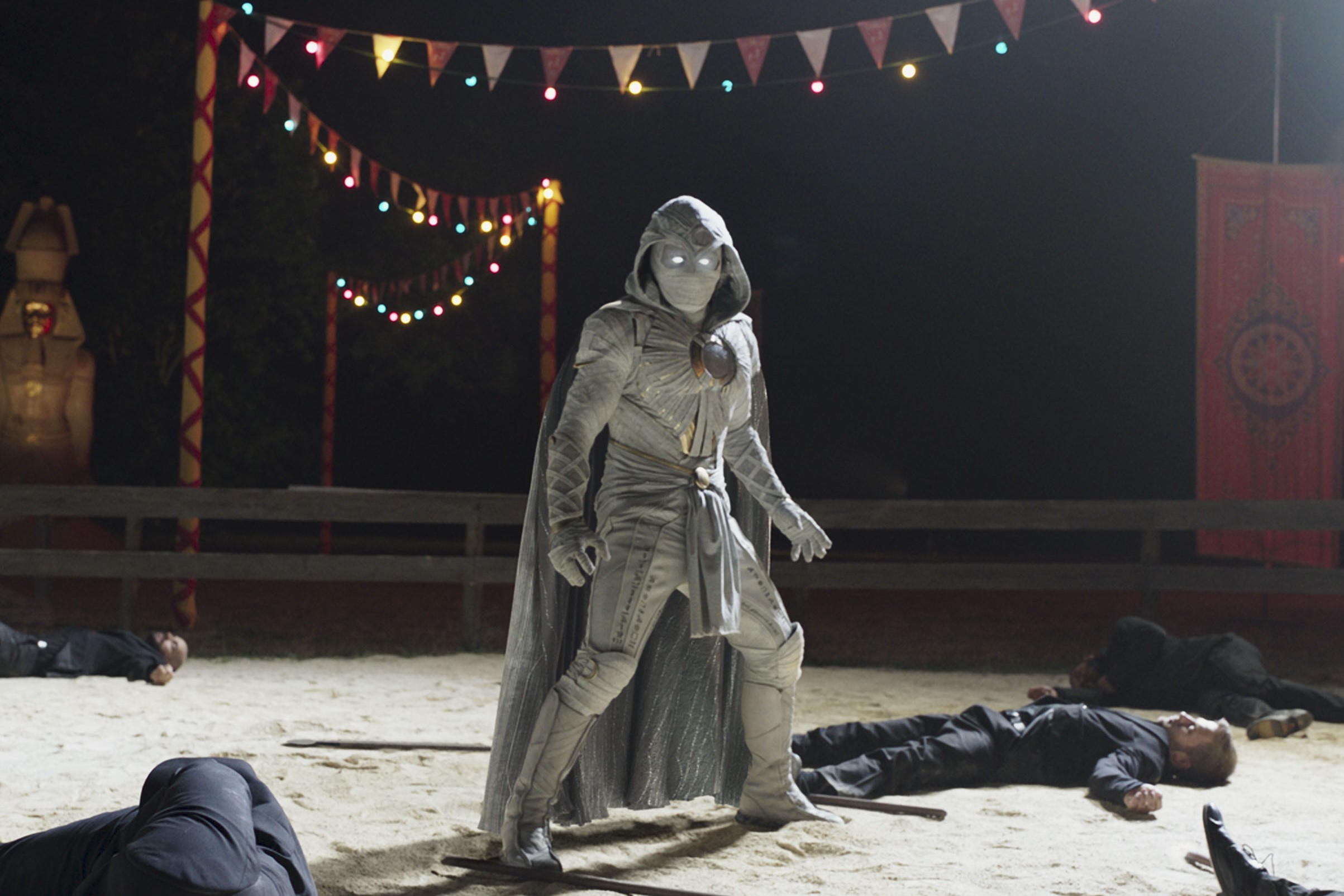 Oscar Isaac, the star of 'Moon Knight,' which has a release date of March 30, wears his white Moon Knight costume as he stands over guys laying unconscious on the ground.