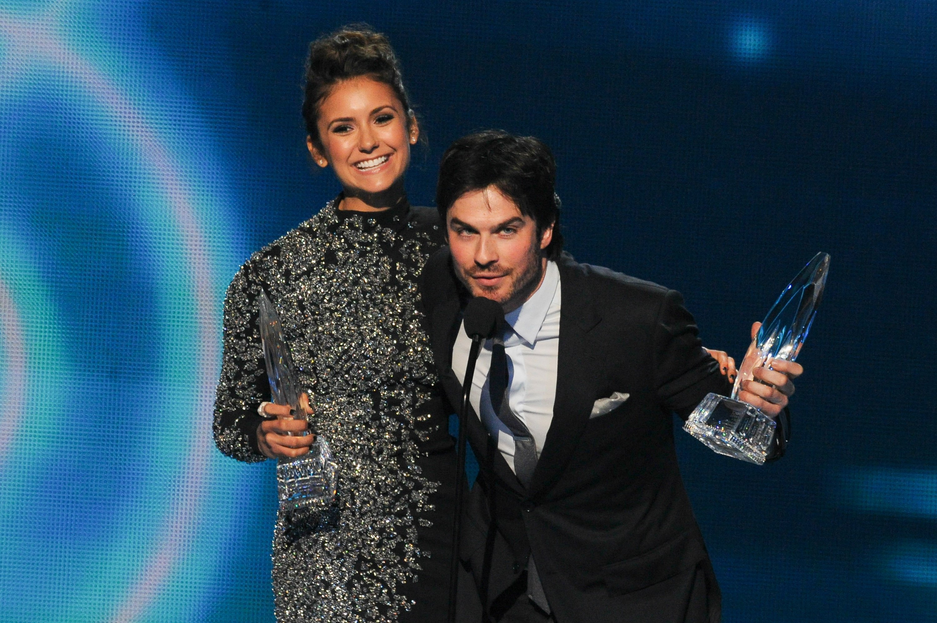 Nina Dobrev and Ian Somerhalder, who played Elena and Damon in 'The Vampire Diaries' series finale, accept an award onstage. Dobrev wears a diamond-studded long-sleeved black dress. Somerhalder wears a black suit over a white button-up shirt and gray tie.