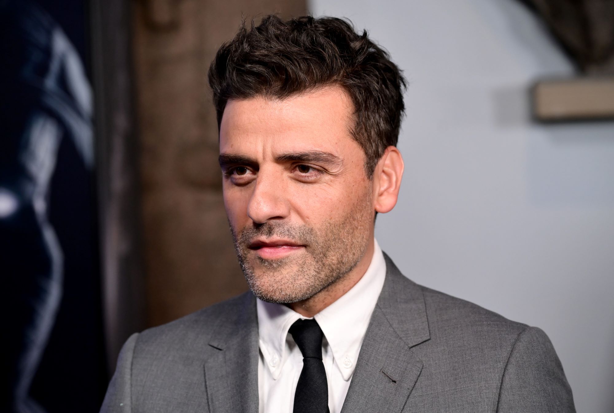 'Moon Knight' star Oscar Isaac wears a gray suit over a white button-up shirt and black tie.