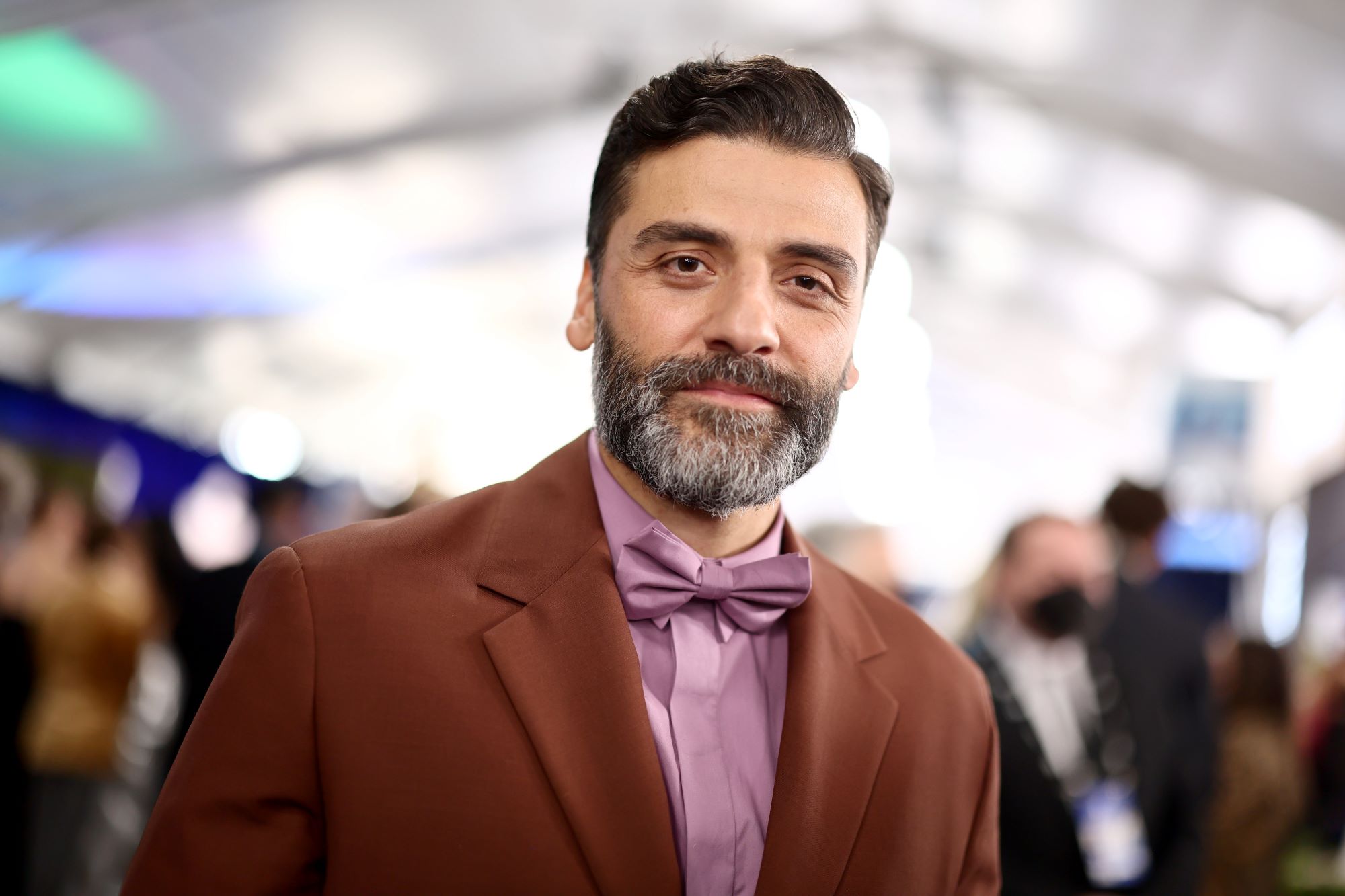 Oscar Isaac, who stars in 'Moon Knight,' wears a brown suit over a light purple button-up shirt and bow tie.