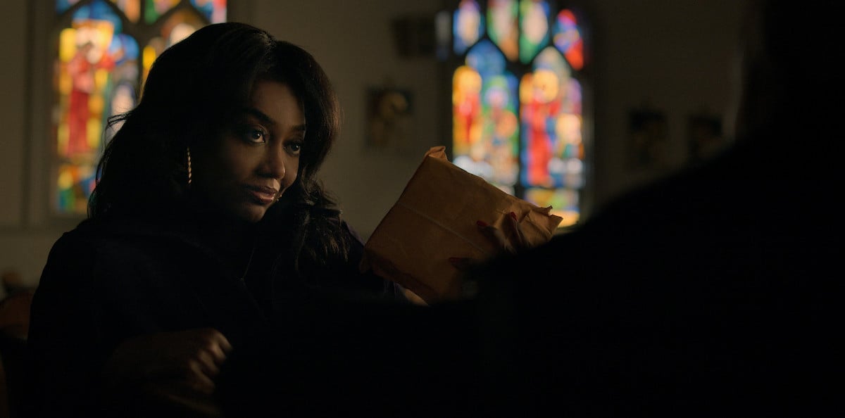 Patina Miller as Raquel "Raq" Thomas wearing all black and standing in a church holding a package in 'Power Book III: Raising Kanan'