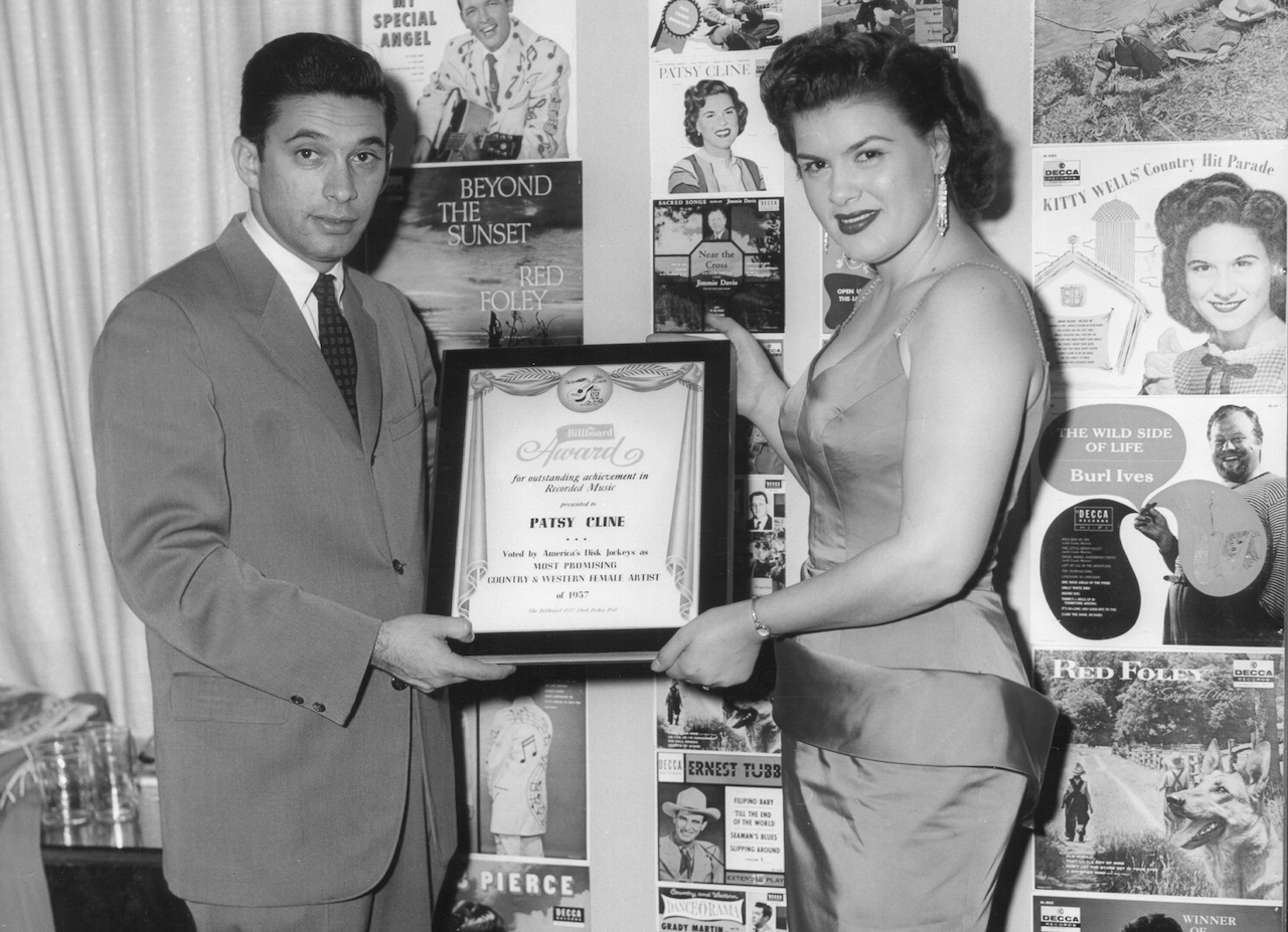 Black and white photo of Patsy Cline in a sleeveless dress, holding a Billboard Award c. 1957
