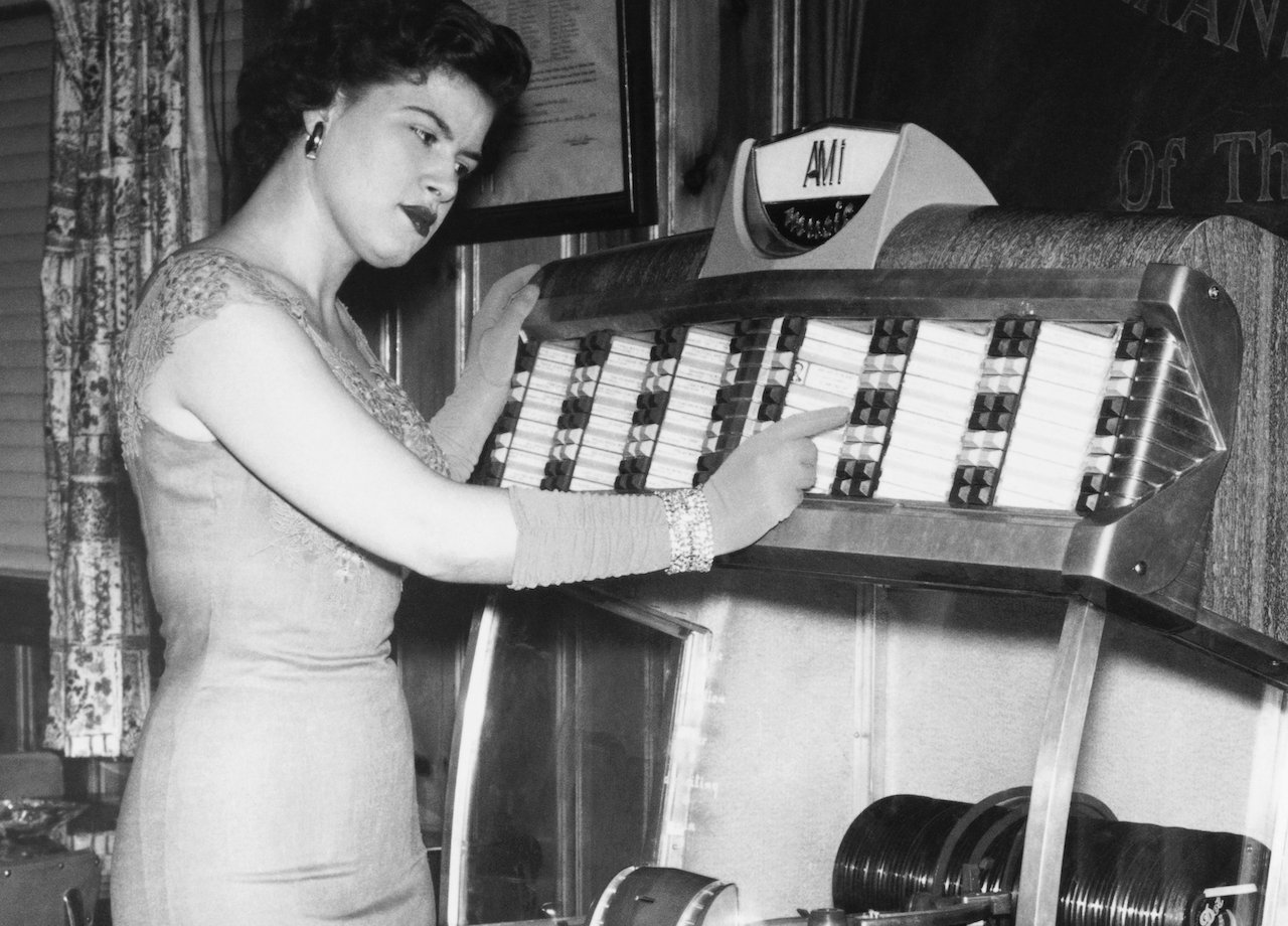 Black and white photo of Patsy Cline in a gown and matching gloves, pointing to a jukebox