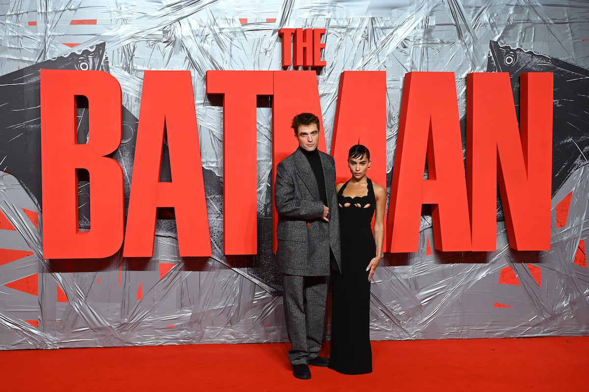 Robert Pattinson and Zoe Kravitz pose in front of a large red sign that says, "The Batman."
