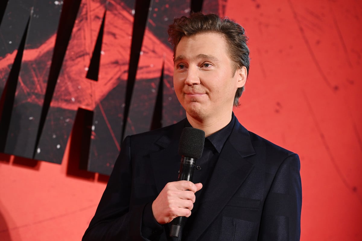Paul Dano wears a black suit and holds a microphone on the red carpet