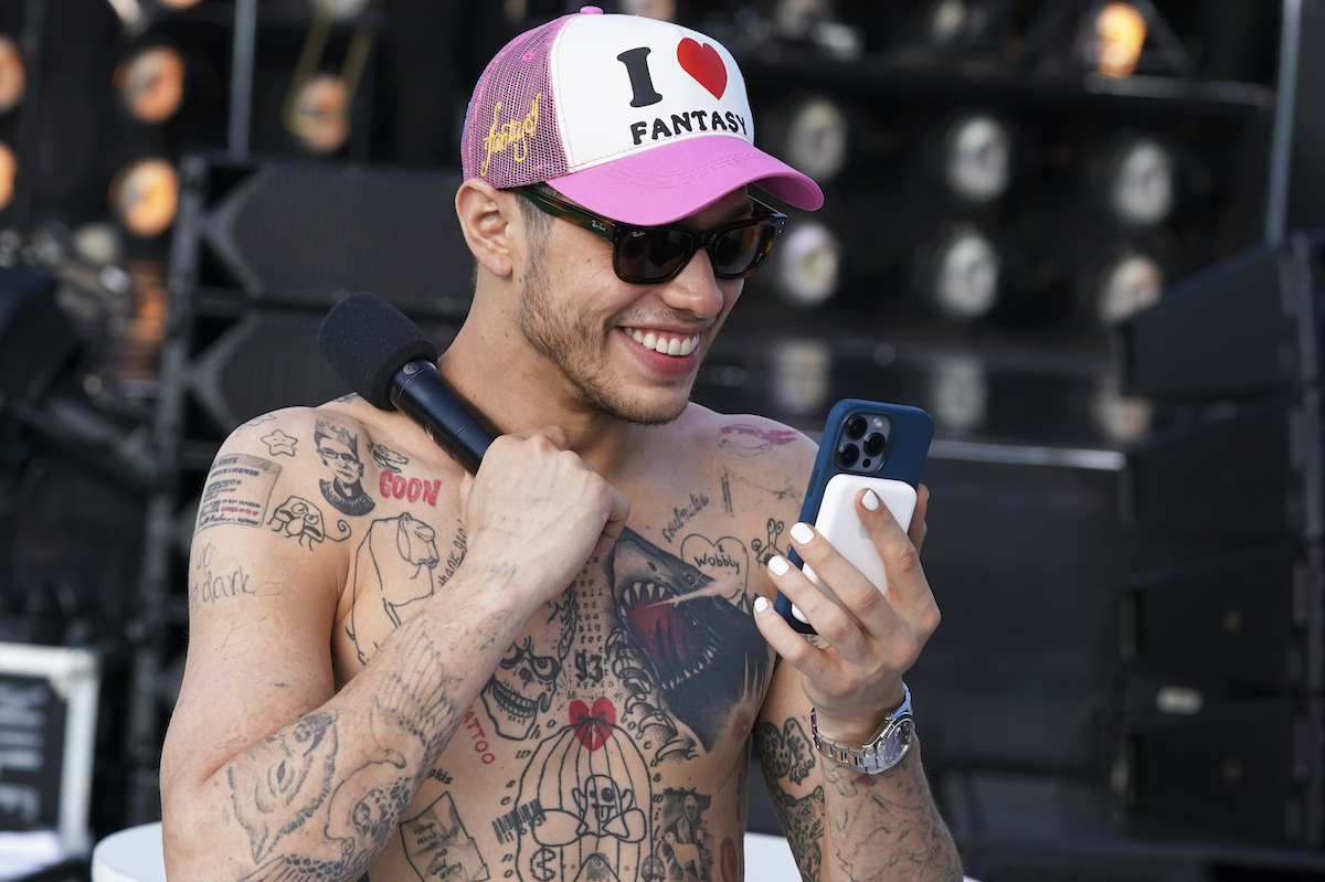 A shirtless Pete Davidson smiles while looking at his phone.