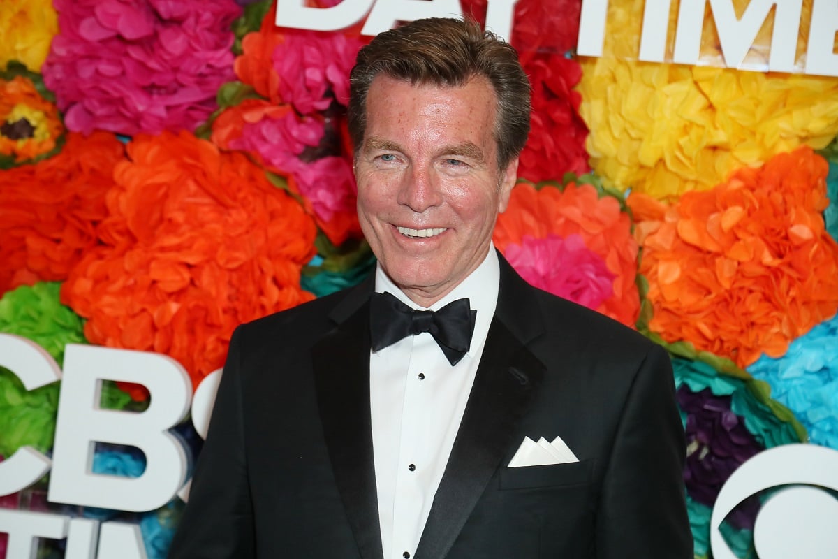 'The Young and the Restless' actor Peter Bergman wearing a tuxedo and standing in front of a floral hedge.