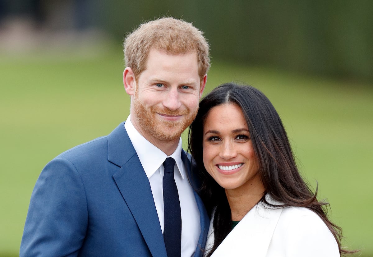 Prince Harry wears a navy blazer standing next to Meghan Markle in a white coat