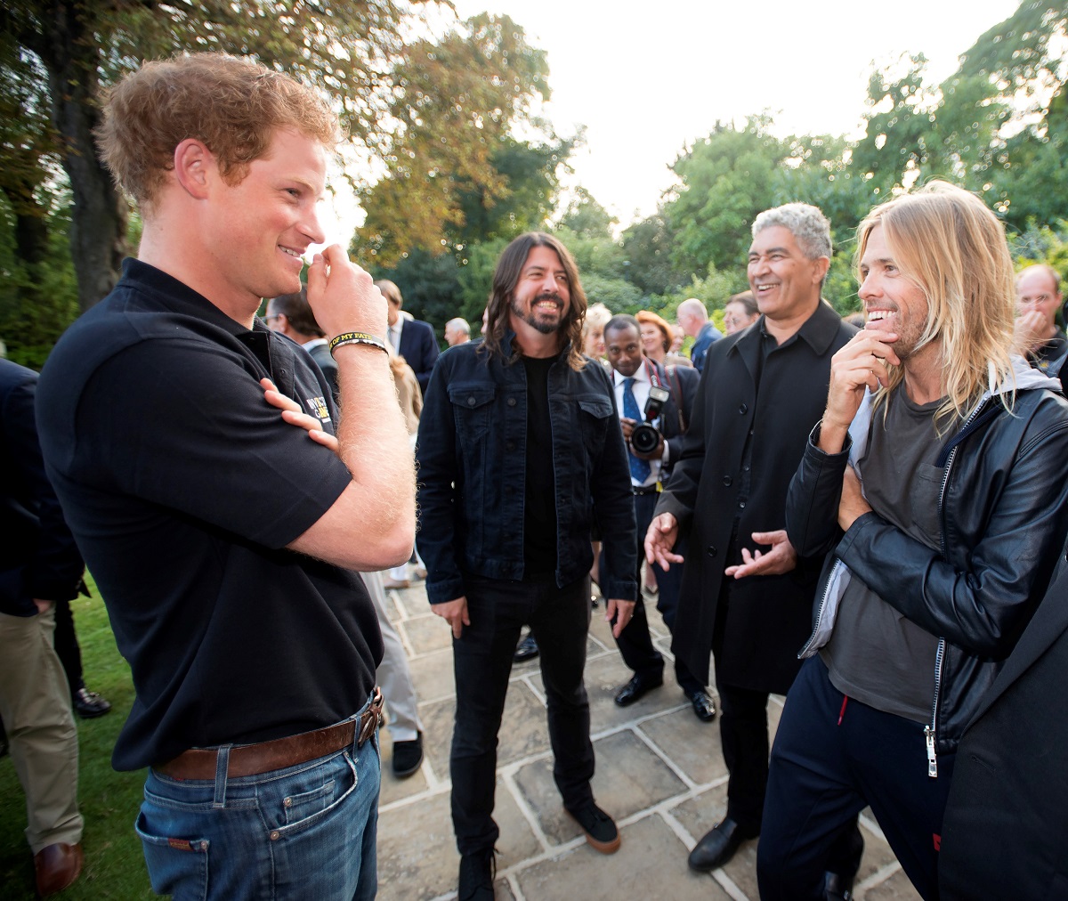Prince Harry speaking outdoors with singer Dave Grohl and drummer Taylor Hawkins of the Foo Fighters