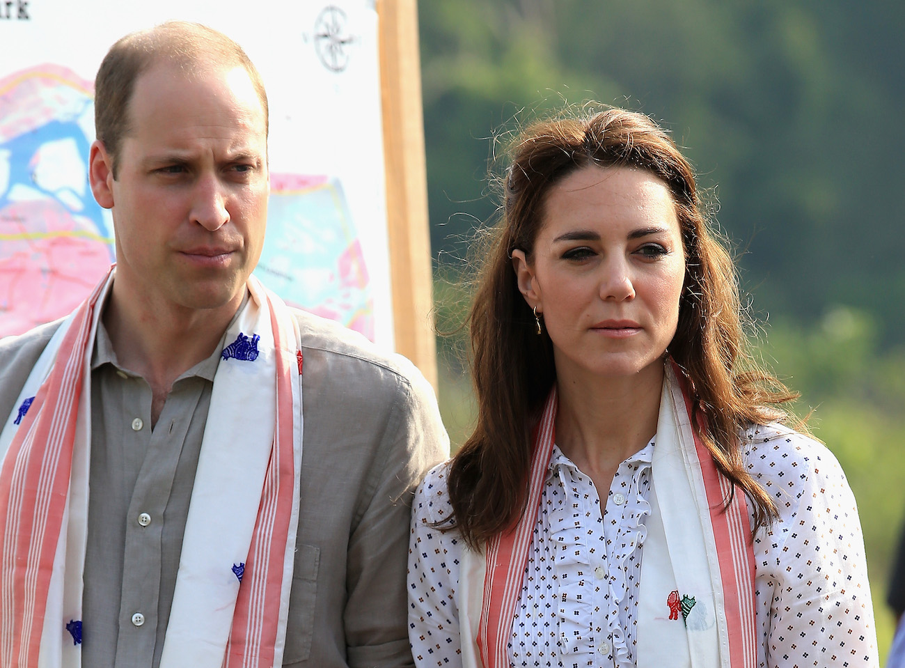 Prince William and Kate Middleton looking on at something off-camera, both wearing red-and-white scarves