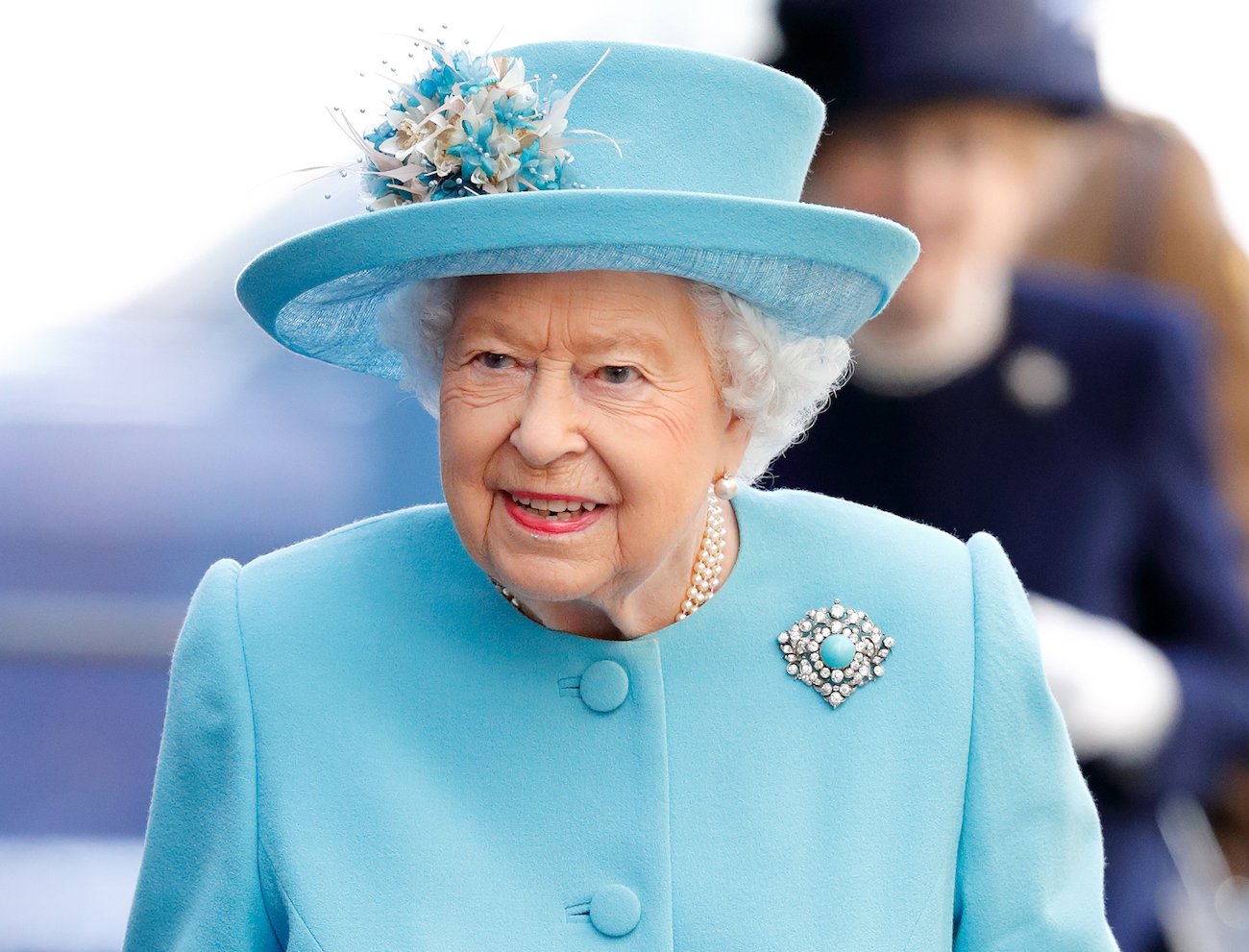 Queen Elizabeth looking on while wearing a blue outfit with a blue hat