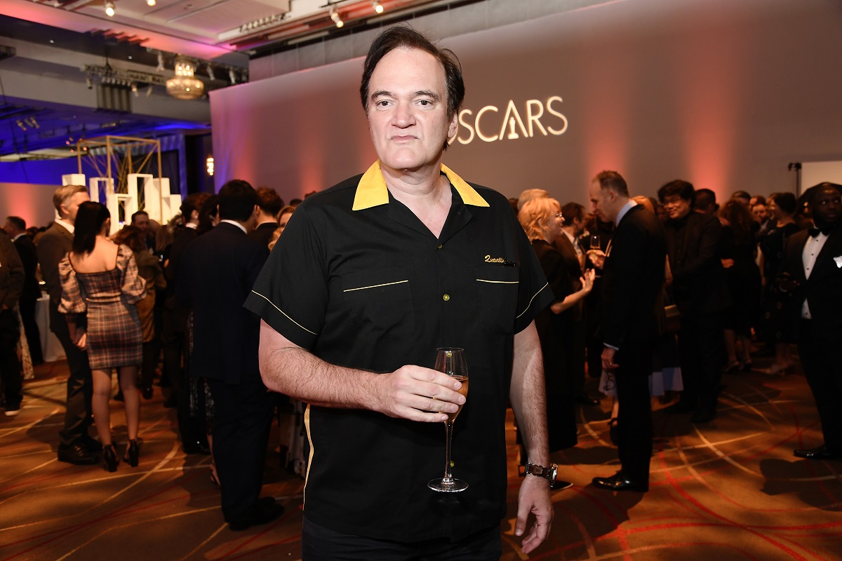 Quentin Tarantino posing while holding a glass and wearing a black shirt.