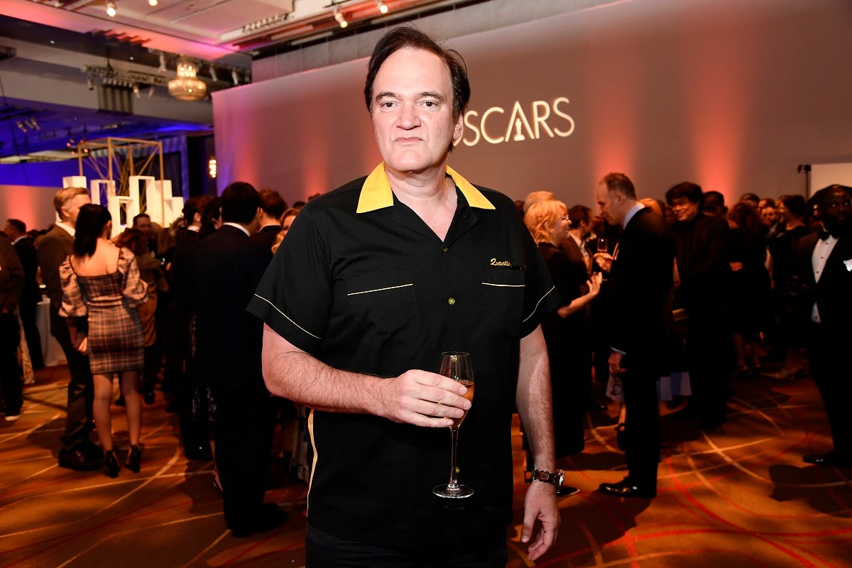 Quentin Tarantino posing while holding a glass and wearing a black shirt.