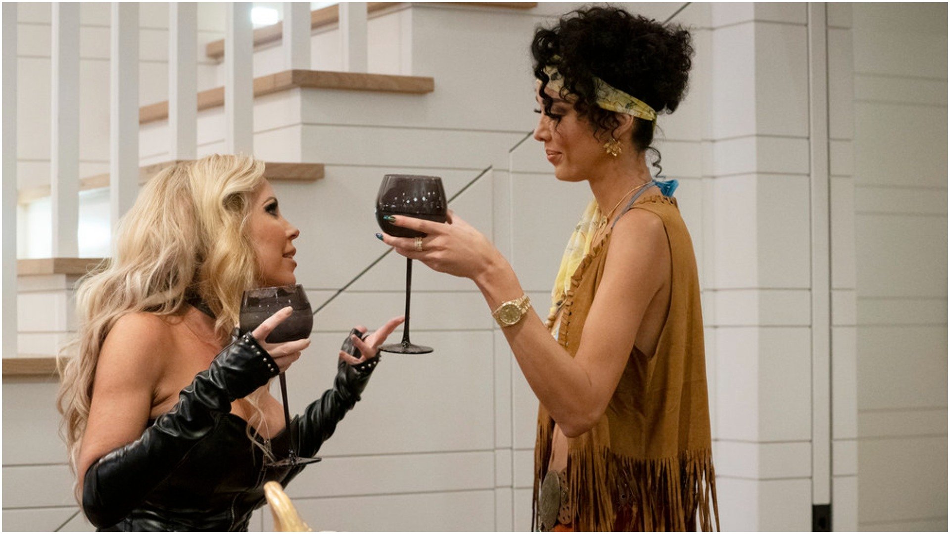Jen Armstrong, Noella Bergener from 'RHOC' dressed in costumes have a conversation while holding a glass of wine 