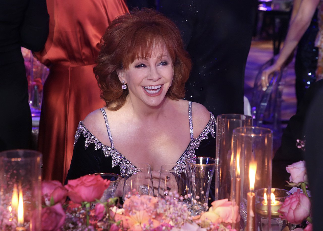 Reba McEntire smiles while seated at a candlelit table, wearing a dark blue dress