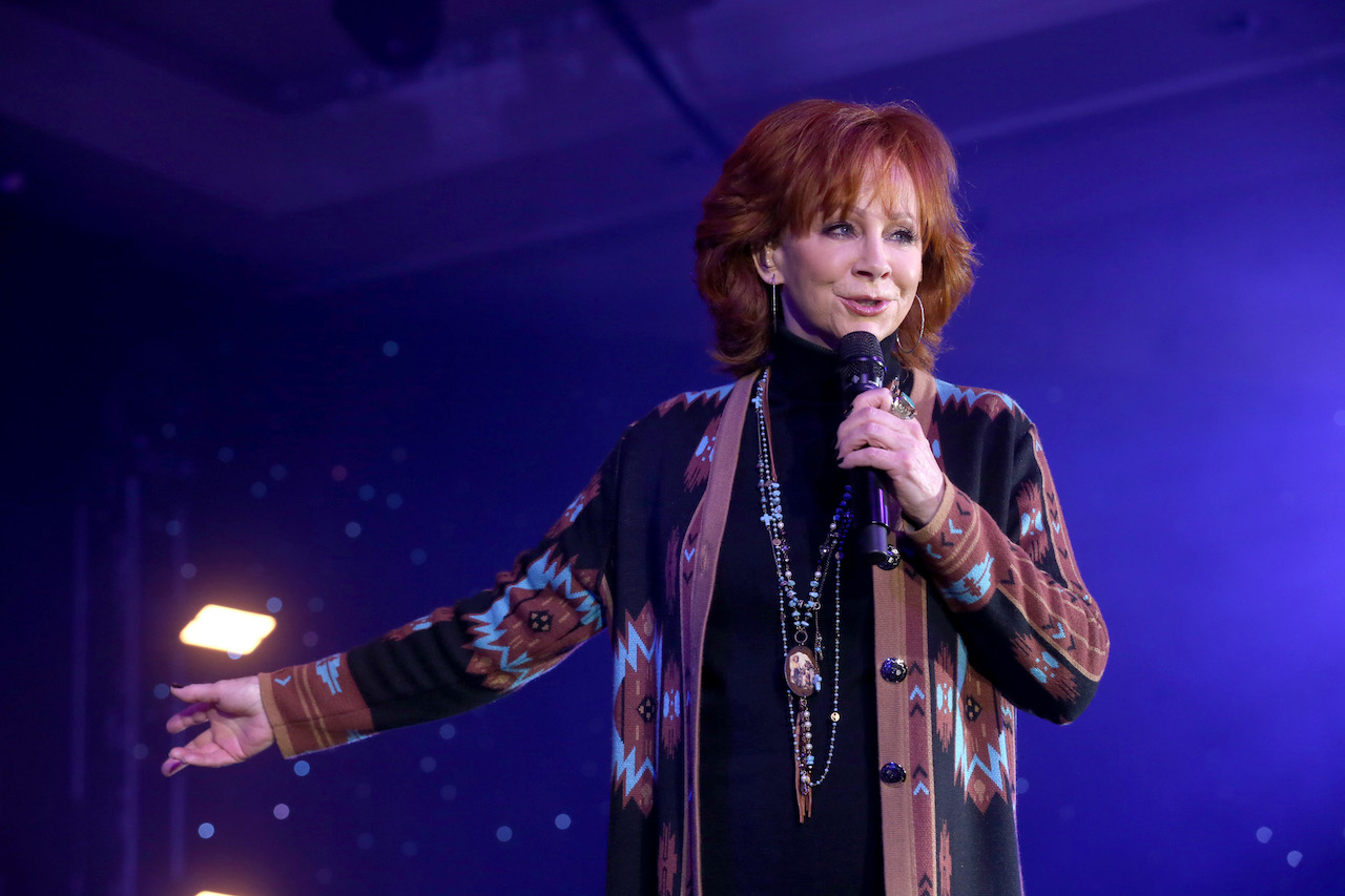 Reba McEntire performs onstage in a printed cardigan and long-hanging necklaces