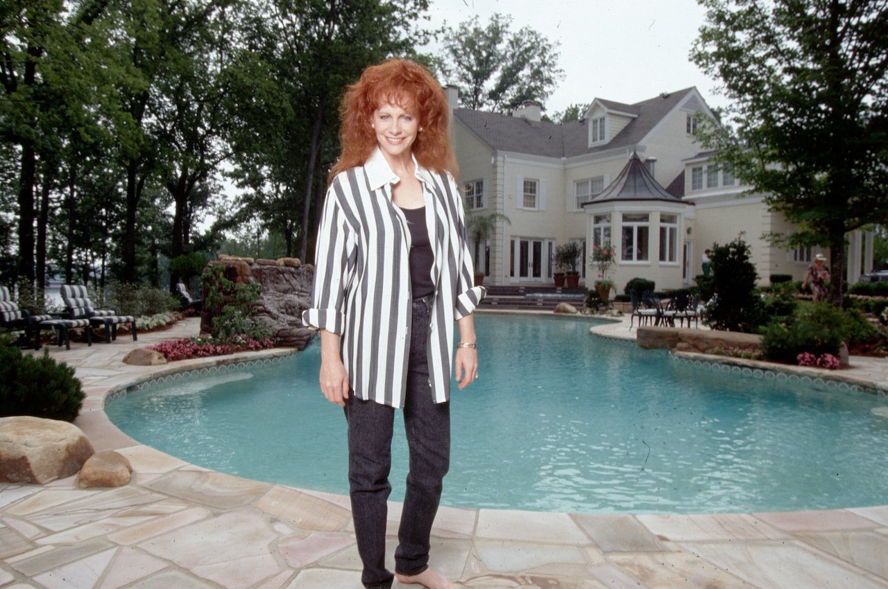 Reba McEntire in a striped shirt and jeans, standing beside the pool at her former mansion, c. 1994