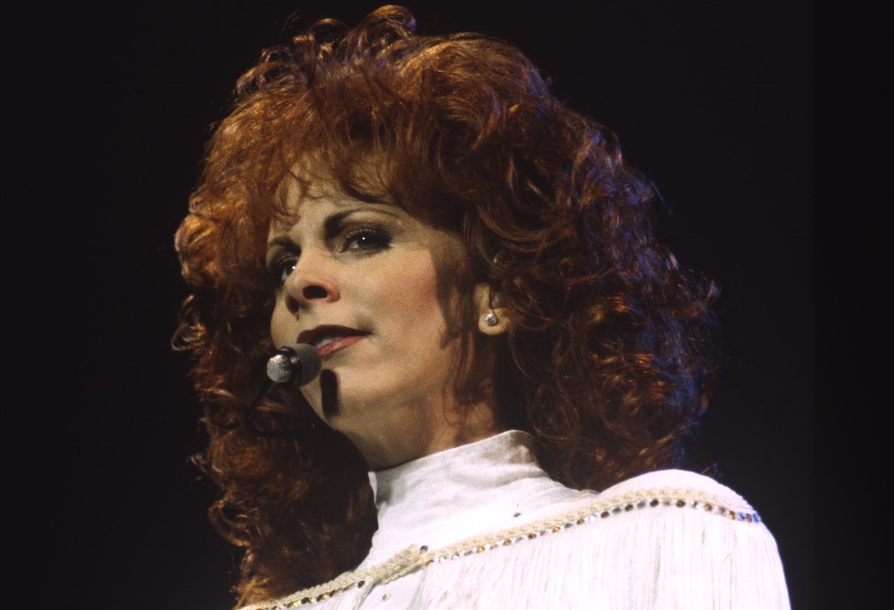 Reba McEntire in white, singing into a microphone c. 1994