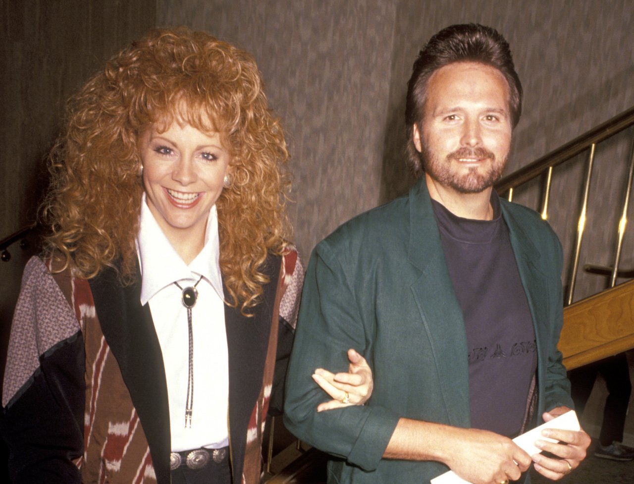 Reba McEntire in a brown jacket, walking arm in arm with Narvel Blackstock, in a green jacket c. 1991