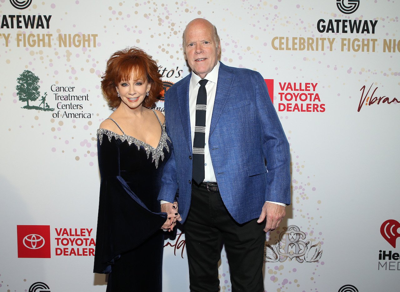 Reba McEntire in a dark blue dress, holding hands with Rex Linn, who is wearing a blue suit jacket and tie