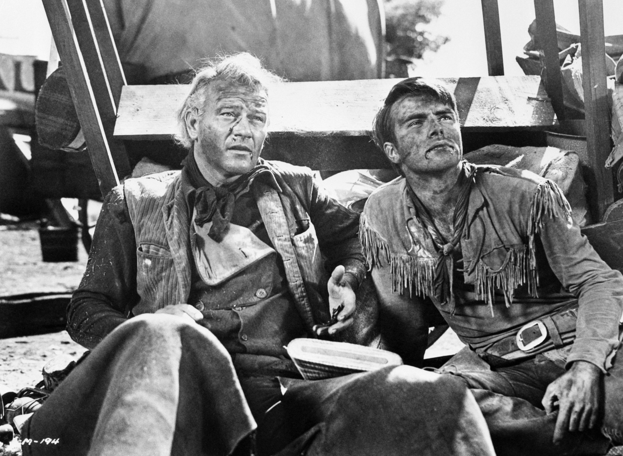 'Red River' actors John Wayne as Thomas Dunson and Montgomery Clift as Matt Garth sitting next to each other beaten up