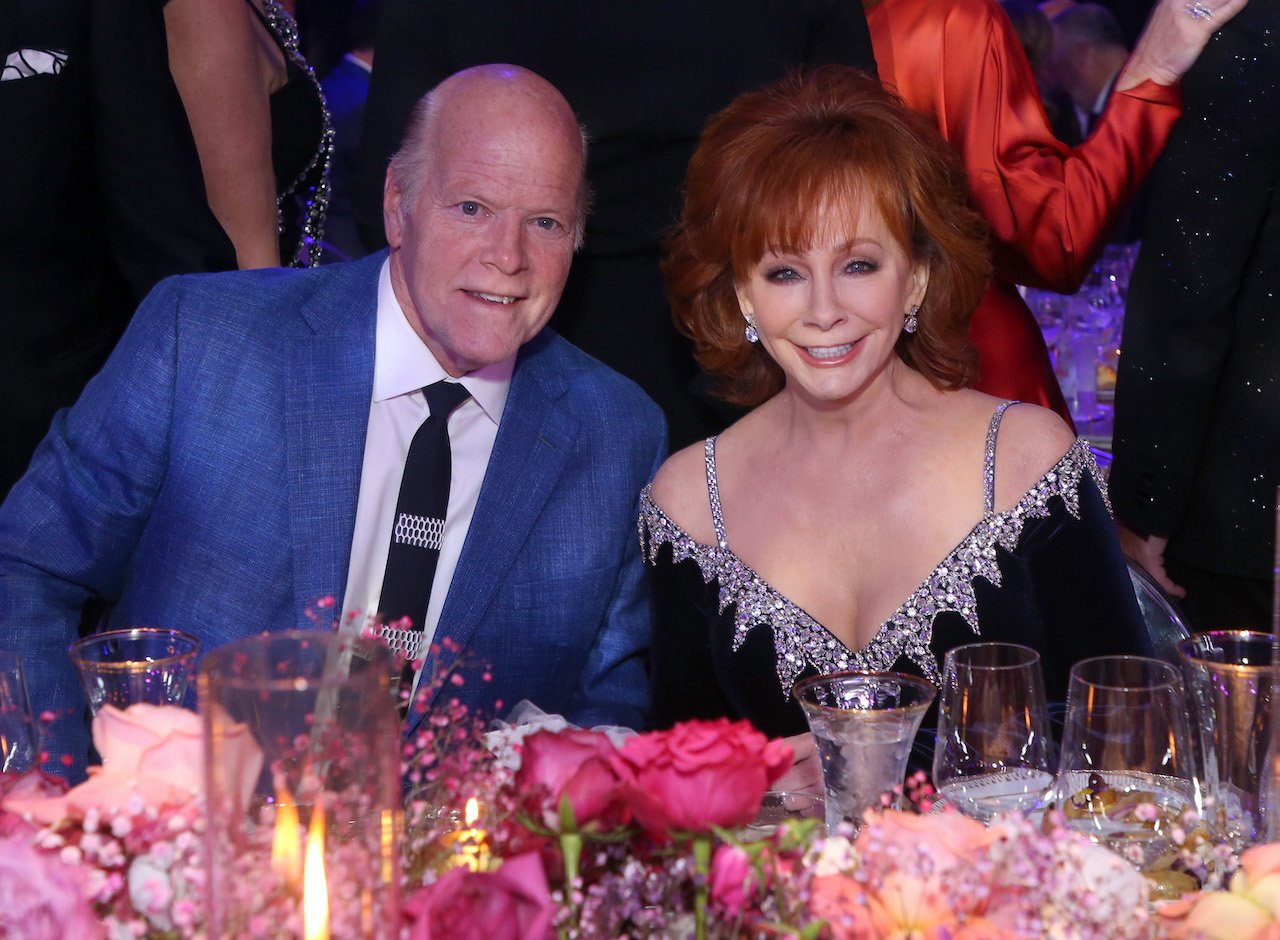 (L-R) Rex Linn in a blue jacket and Reba McEntire in a dark blue dress, seated at a table and smiling