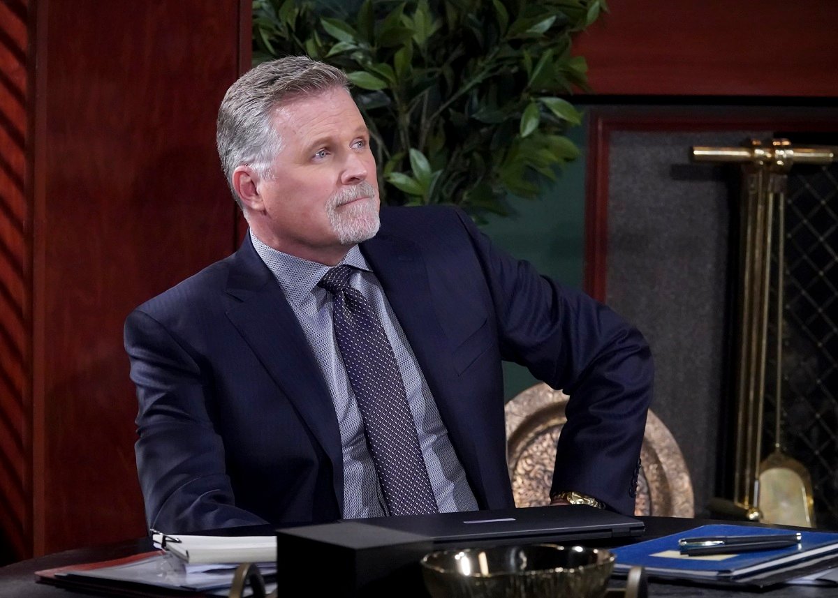 'The Young and the Restless' actor Robert Newman wearing a blue suit and sitting at a desk in the Newman Enterprises office.