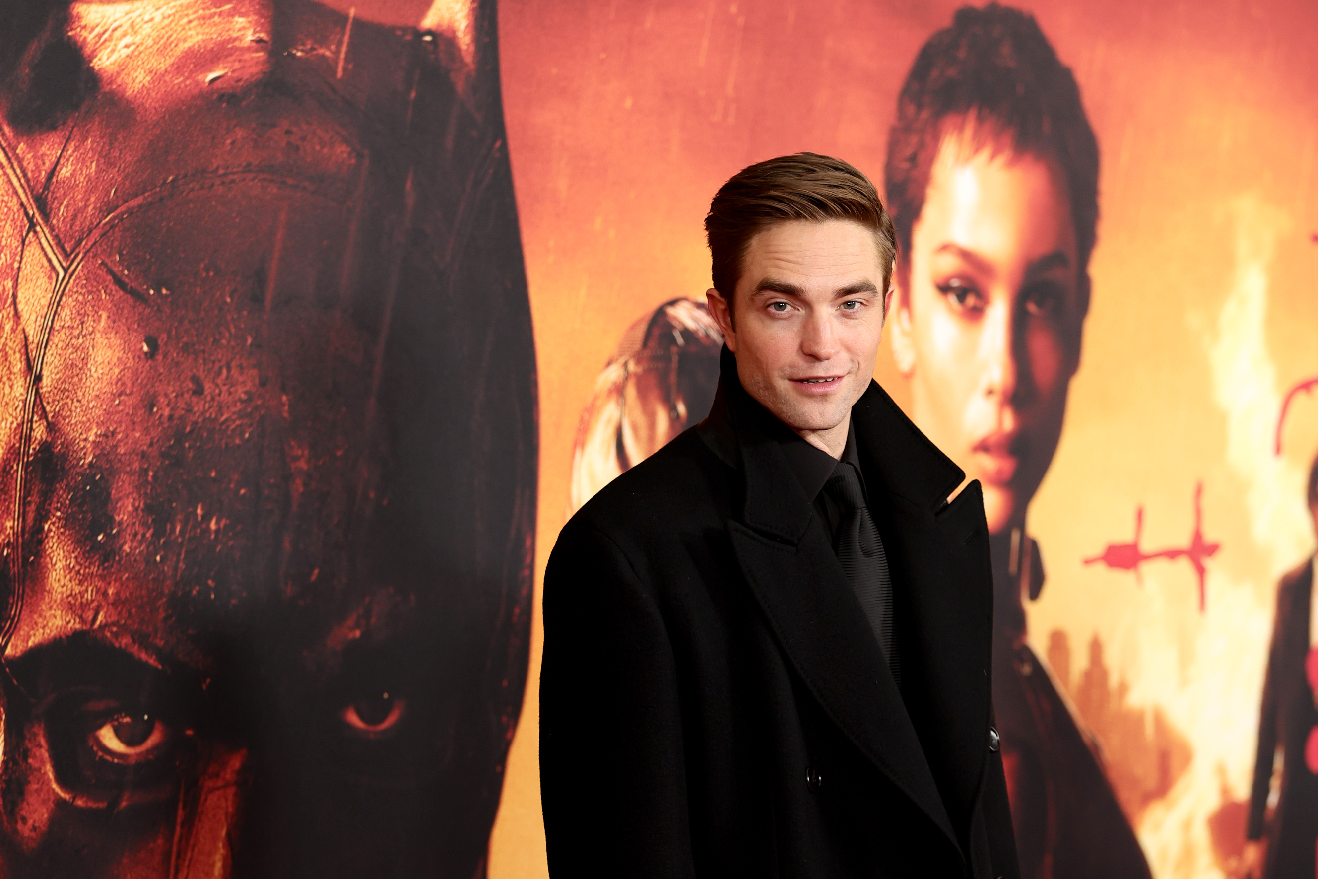 'Twilight' and 'The Batman' star Robert Pattinson. He's wearing a black coat and standing in front of an image for 'The Batman.'
