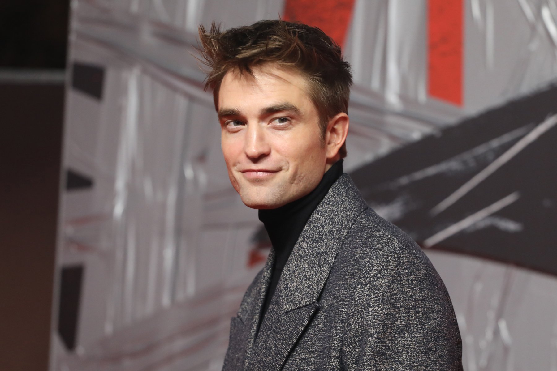 Robert Pattinson at a screening of 'The Batman.' He's wearing a long grey coat and smiling.