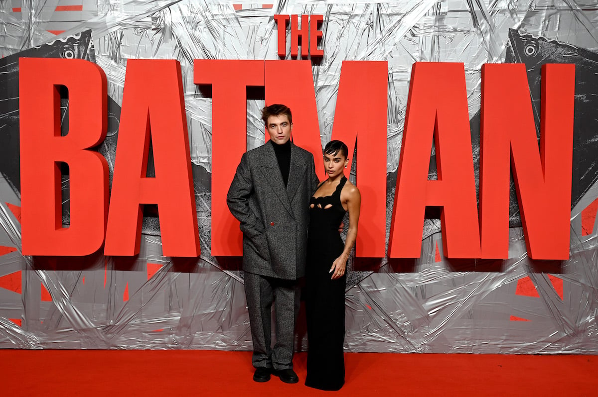 Robert Pattinson and Zoe Kravitz pose in front of a red sign that says "The Batman."